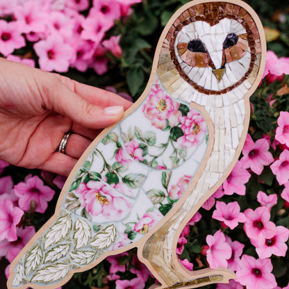 Decorative owl-shaped mosaic with floral patterns held in front of pink flowers