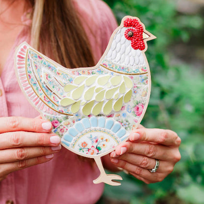 Woman holding a colorful ceramic chicken figurine against a green outdoor background