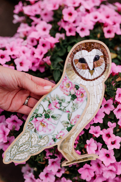 Decorative owl-shaped mosaic with floral patterns held in front of pink flowers